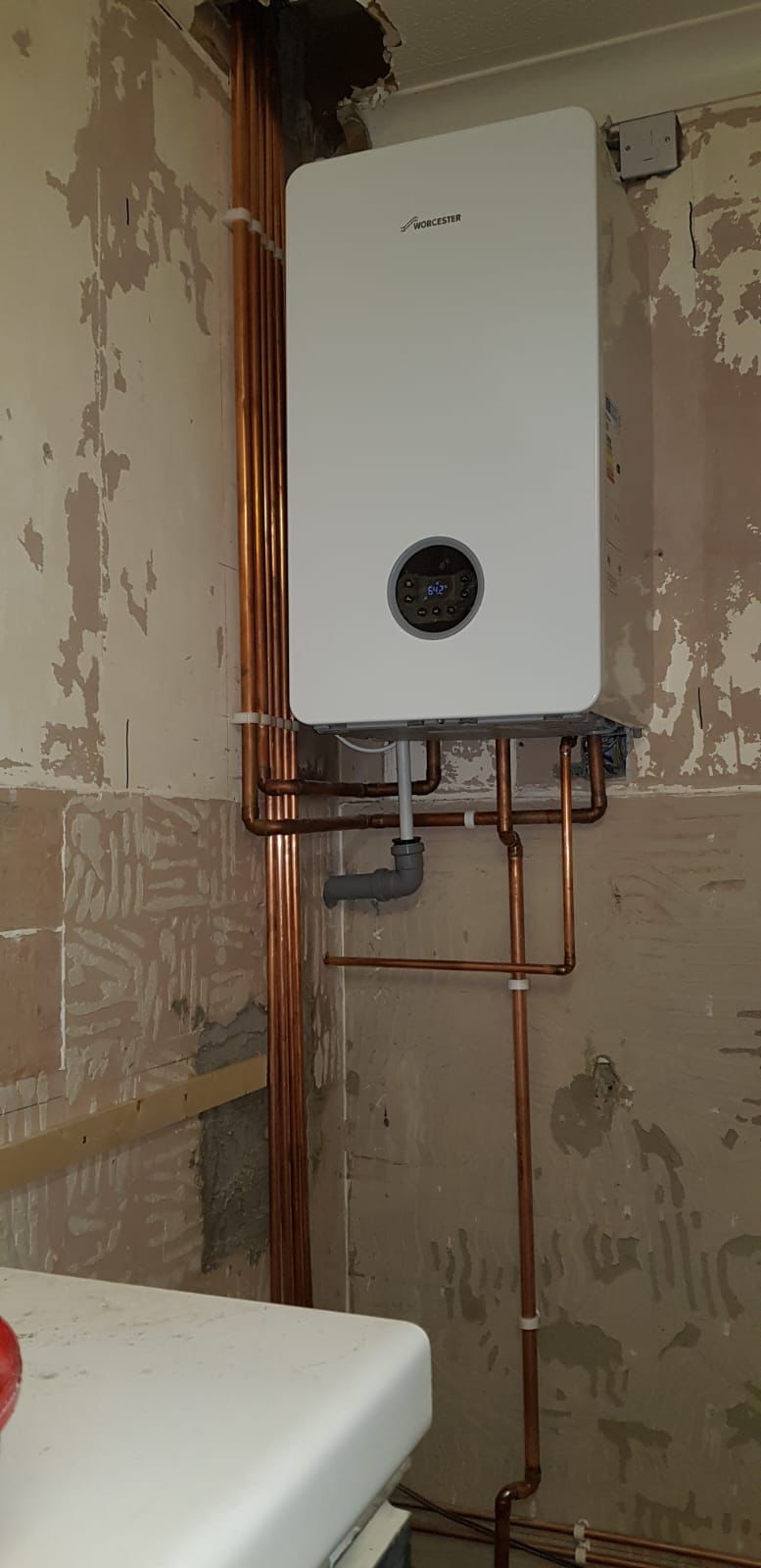 Worcester Bosch boiler installed on a bare plaster utility room wall with new copper pipes